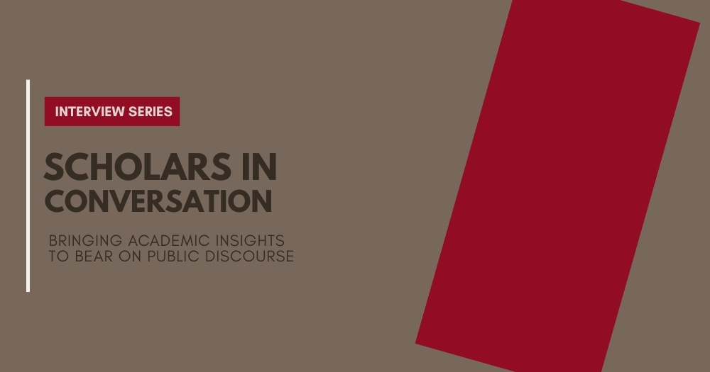 A plain brown background with a red vertical strip on the right. There is the text of the left saying: Scholars in Conversation - Bringing academic insights to bear on public discourse